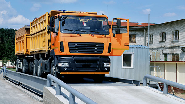 Oranger Lastwagen auf einer Fahrzeugwaage in einem Wertstoffhof – Recycling und Entsorgungslogistik.